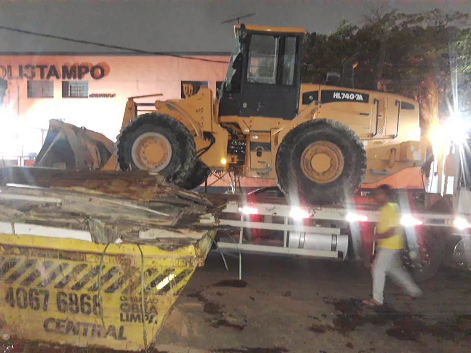 Pá carregadeira sobre caminhão e caçamba em operação noturna