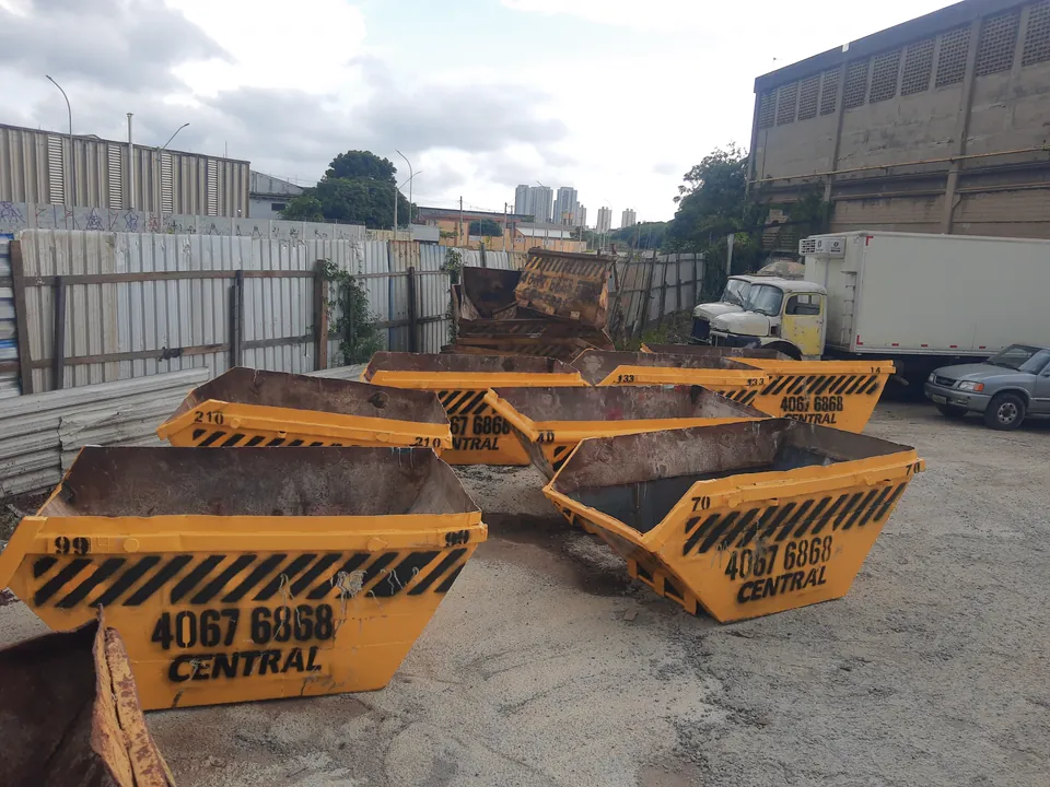 Caçambas no pátio da empresa com caminhão ao fundo